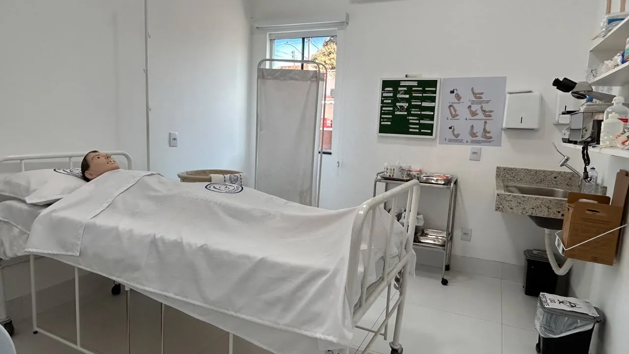 Laboratorio de enfermagem com leito hospitalar, carrinho de materiais, pia e biombo