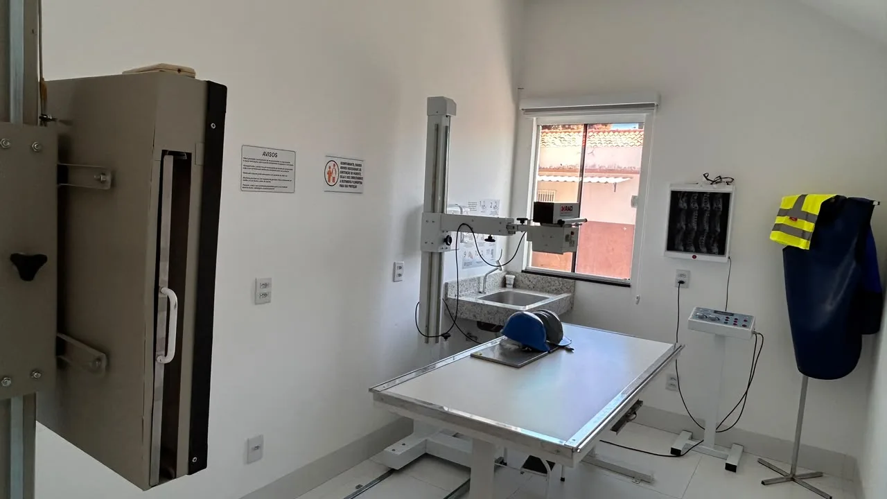 Laboratorio de radiologia com aparelho de raios X, mesa de exame, negatoscopio e avental de chumbo