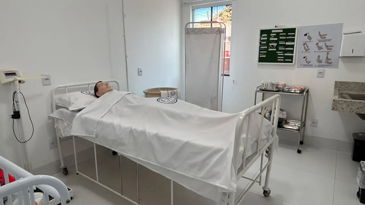 Manequim de simulacao em leito hospitalar no laboratorio de enfermagem, com balanca e carrinho de curativo