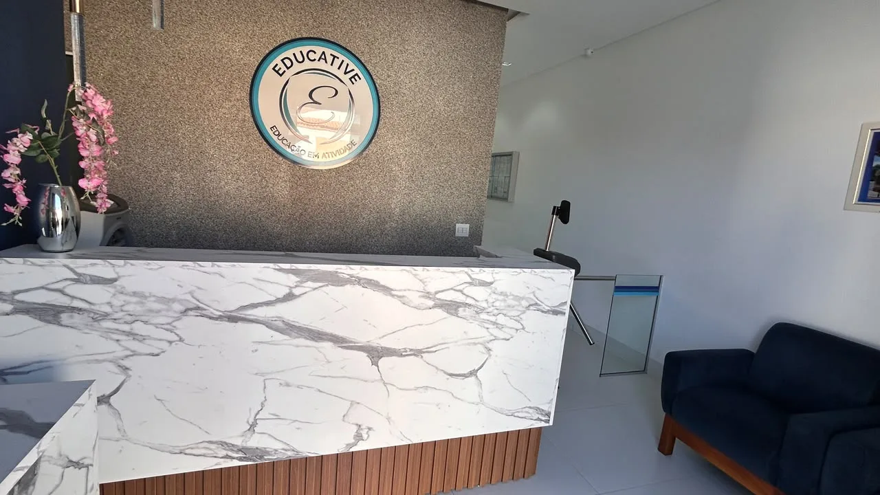 Recepcao da filial com balcao de marmore, logotipo da Educative na parede e sofa de espera