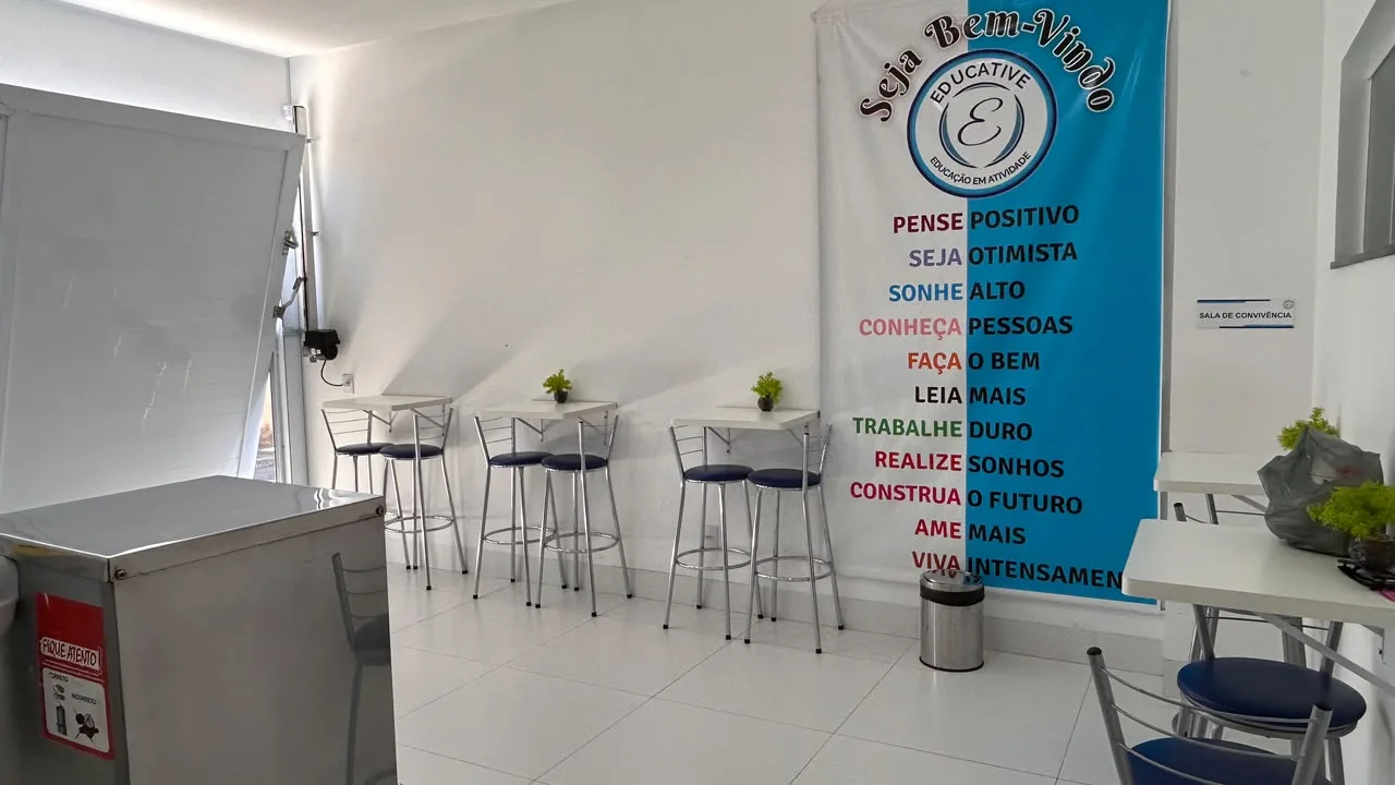 Sala de convivencia com banquetas, mesas de apoio e banner de boas-vindas da Educative
