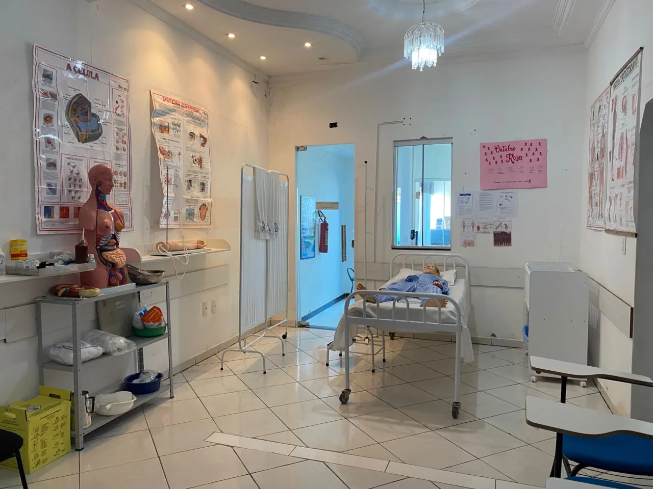 Outro angulo do laboratorio de enfermagem, com biombo, suporte de soro e bancada de materiais