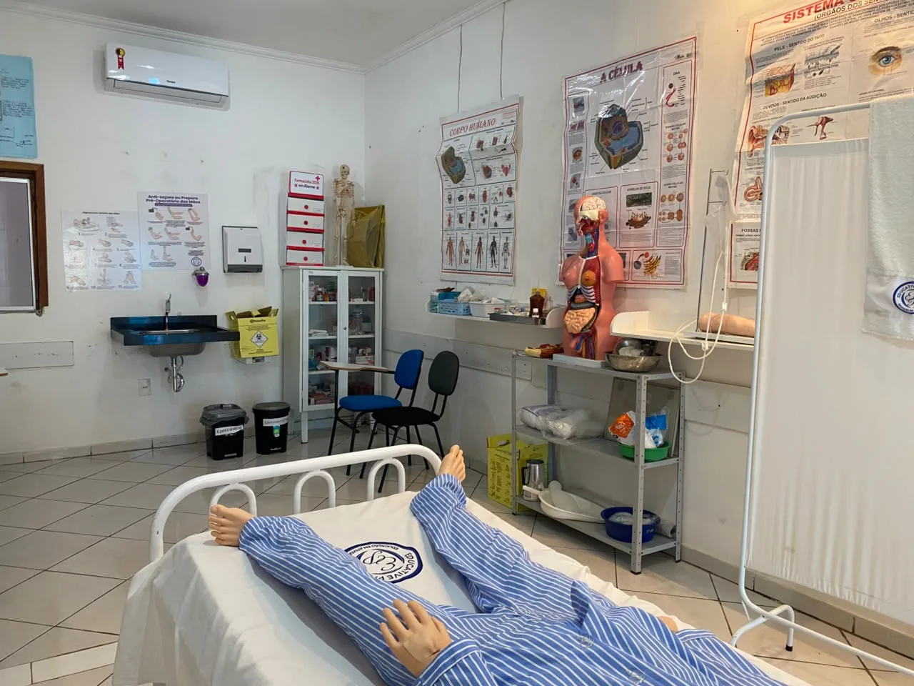 Manequim de simulacao em leito hospitalar no laboratorio de enfermagem, ao lado de armario de materiais