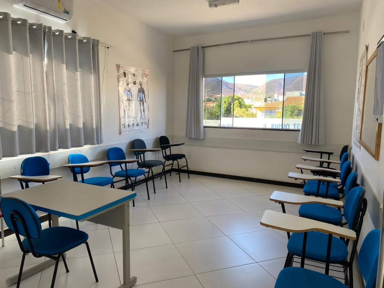 Sala de aula climatizada com carteiras, mesa de apoio e paineis de anatomia